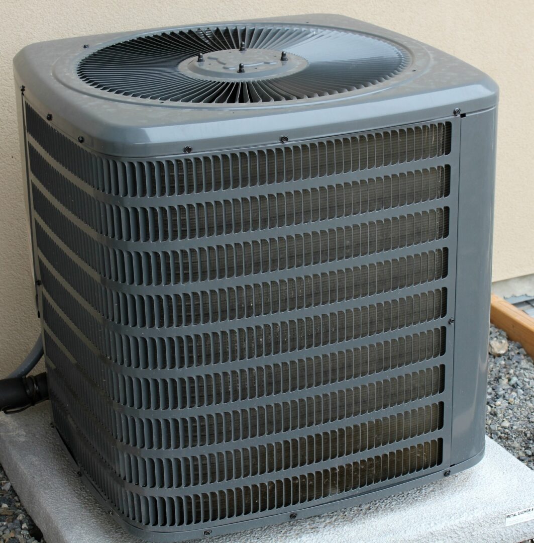 Outdoor air conditioning unit situated on a concrete pad against a beige wall.