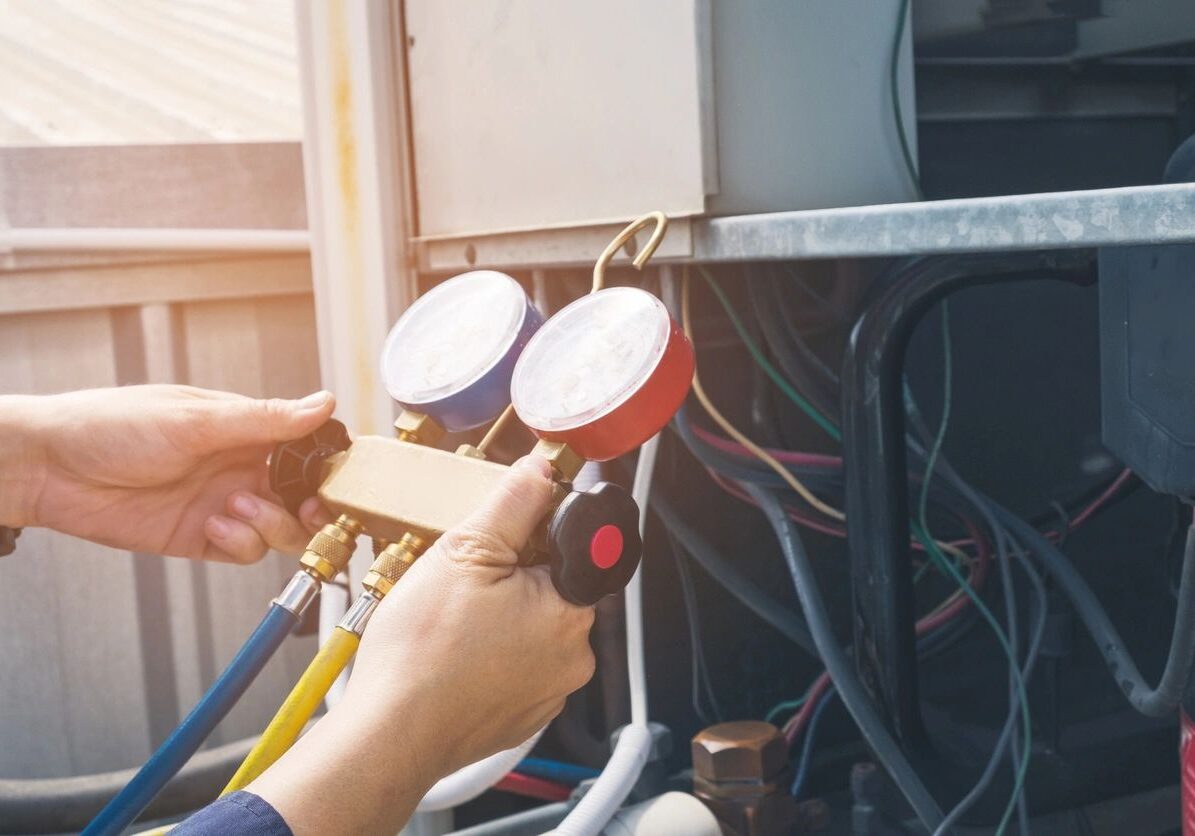 A person holding a pressure gauge while performing maintenance on an HVAC system with various colored hoses attached.